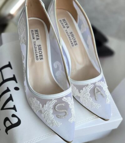 کفش عروس دانتل تکست‌دار با نام عروس و داماد نمای نزدیک کفش عروس دانتل تکست‌دار مدل اختصاصی کفش عروس سفید دانتل مناسب عکاسی و فرمالیته جزئیات دانتل و نوشته روی کفش عروس تکست‌دار ست عروس با کفش دانتل تکست‌دار هیوا روی زمین عکاسی شده